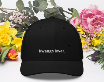 May include: A black trucker hat featuring a mesh back and a solid front panel. The front of the hat displays the white embroidered text "kwanga lover." in a simple, lowercase sans-serif font, centered above the curved brim of the cap.