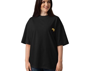 May include: A black short-sleeved t-shirt featuring a small, gold-colored embroidered graphic of the continent of Africa positioned on the left side of the chest. The garment has a crew neckline and a loose, relaxed fit with wide sleeves.
