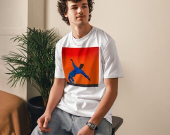 May include: White t-shirt featuring a graphic of a person in a blue outfit against a red and orange background. The person is in a dynamic pose. The t-shirt is being worn by a person.
