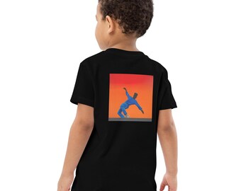 May include: Black t-shirt featuring a graphic of a person in a blue outfit against an orange and red background. The image is on the back of the shirt. The shirt is being worn by a child.