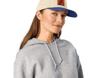 May include: A beige and blue baseball cap with a flat brim. The cap features a rectangular patch with an orange background and a blue silhouette of a person. The person is wearing a gray hoodie.