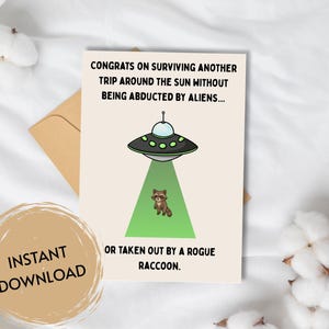 May include: Greeting card with a cartoon illustration of a UFO beaming a raccoon. The card reads, "Congrats on surviving another trip around the sun without being abducted by aliens... or taken out by a rogue raccoon."