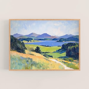 May include: Landscape painting in a light wood frame. The artwork depicts a serene scene with a blue lake, rolling green hills, and distant mountains under a blue sky. A path winds through the foreground.