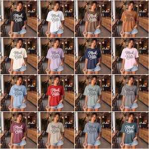 May include: A collection of sixteen short-sleeve crew neck t-shirts in various solid colors, each featuring the text Mock Vista printed in a cursive script on the front. The shirts are displayed in a grid format, showcasing different color options.