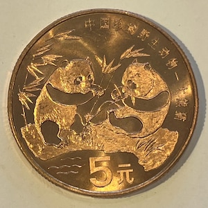 May include: A circular bronze-colored coin featuring two pandas eating bamboo stalks. The coin displays the Chinese characters for wildlife and the number 5 followed by the character for yuan at the bottom. The design is embossed with a metallic finish.