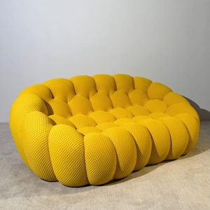 Könnte beinhalten: Ein modernes, gelbes Sofa mit einem einzigartigen, strukturierten Design. Das Sofa besteht aus einer Reihe von abgerundeten, miteinander verbundenen Kissen, die eine optisch ansprechende und komfortable Sitzanordnung schaffen. Die leuchtend gelbe Farbe verleiht jedem Wohnraum Lebendigkeit.