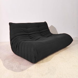 Könnte beinhalten: Ein schwarzes Zweisitzer-Sofa im modernen Stil. Das Sofa hat eine niedrige, abgerundete Form und einen strukturierten, gerippten Stoff. Die Rückenlehne ist getuftet, und das Gesamtdesign ist minimalistisch und modern.