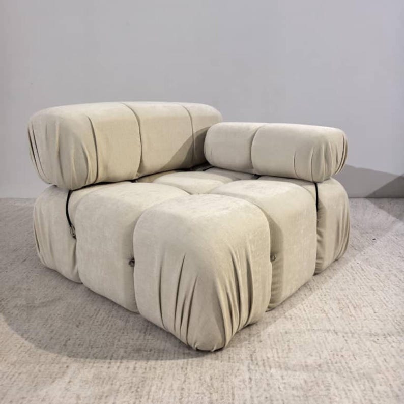 May include: A modular, cream-colored sofa with a unique, rounded design. The sofa is composed of several individual, upholstered blocks, creating a comfortable and stylish seating arrangement. The fabric appears soft and inviting, perfect for a modern living space.