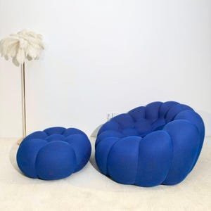May include: A contemporary blue fabric armchair and footstool set. The rounded, modular design of the furniture creates a unique aesthetic. A decorative feather floor lamp stands in the background.