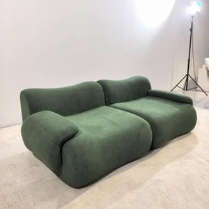 Puede incluir: Un sofá verde bosque de dos piezas con bordes redondeados y una textura suave y aterciopelada. El sofá tiene un diseño moderno con un perfil bajo y una apariencia cómoda. Los brazos y el respaldo son curvos.