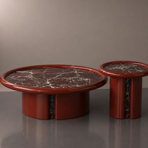 Könnte beinhalten: Ein Set aus zwei modernen Tischen. Der größere Tisch ist oval, der kleinere rund. Beide haben eine rotbraune Oberfläche und eine marmorähnliche Tischplatte. Die Tische sind minimalistisch gestaltet und für ein Wohnzimmer geeignet.