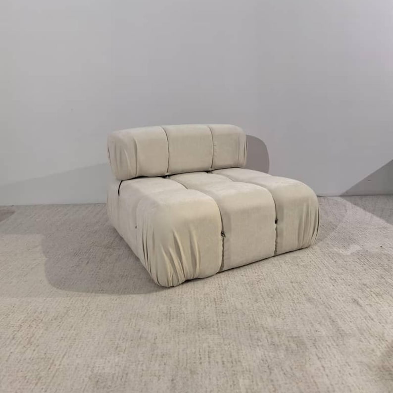 May include: A cream-colored, modular sofa with a rounded, blocky design. The sofa is upholstered in a soft, textured fabric and features a low profile. The design includes a separate backrest cushion, and the overall aesthetic is modern and minimalist.