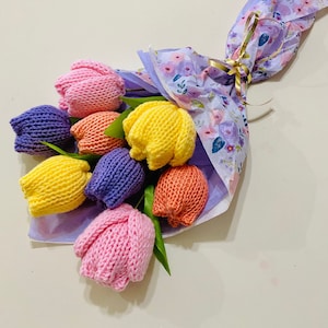 May include: A bouquet of knitted tulips in pink, yellow, orange, and purple, wrapped in floral patterned tissue paper.