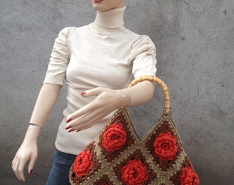 May include: A crochet bag with a brown and orange floral pattern. The bag has a bamboo handle and is made with a granny square stitch.