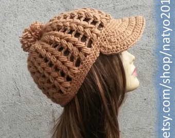 May include: A crocheted hat with a brim and a pom-pom on top. The hat is a light brown color and has a lacy pattern. The hat is being worn by a person with long brown hair. The text "Pattern" is visible at the top of the image. The text "www.etsy.com/shop/natyo2010" is visible on the right side of the image.