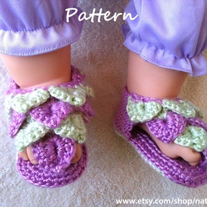 May include: A pair of crocheted baby sandals in purple and green. The sandals feature a flower design and are made with a soft yarn.