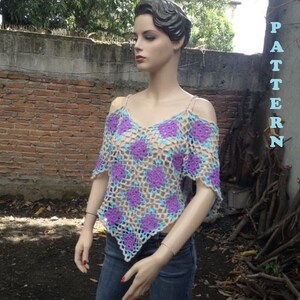 Pode incluir: Um top de croch&ecirc; com um padr&atilde;o roxo, azul e bege. O top tem um decote quadrado e uma forma triangular. O top &eacute; usado por um manequim com jeans azul.