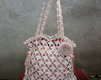 Peut inclure: Un sac cabas en crochet avec une doublure en satin rose et une fleur rose en guise d'embellissement. Le sac a une anse en crochet blanc et un bord festonné.