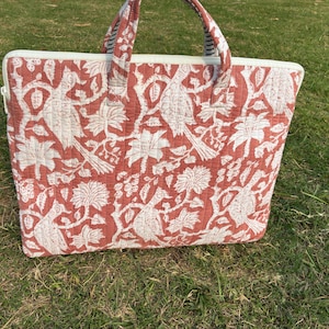 May include: A rectangular tote bag with a red and white bird and floral pattern. The bag has a zipper closure and two handles. The bag is sitting on green grass.