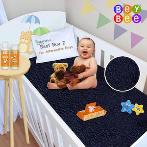 Puede incluir: Una cuna azul marino con un colchón a juego. Un bebé está sentado en la almohadilla, sosteniendo dos osos de peluche. Una almohada con texto, aceite para bebés, talco para bebés y juguetes también están en la cuna. El logotipo de Bey Bee está en la esquina superior derecha.