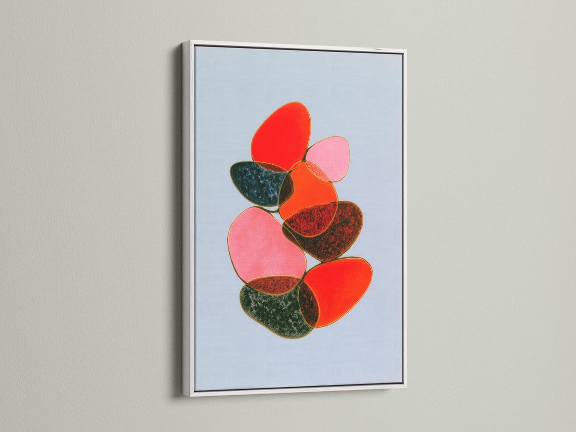 Room mockup showing a framed abstract artwork with overlapping red, pink and green shapes on a light blue background