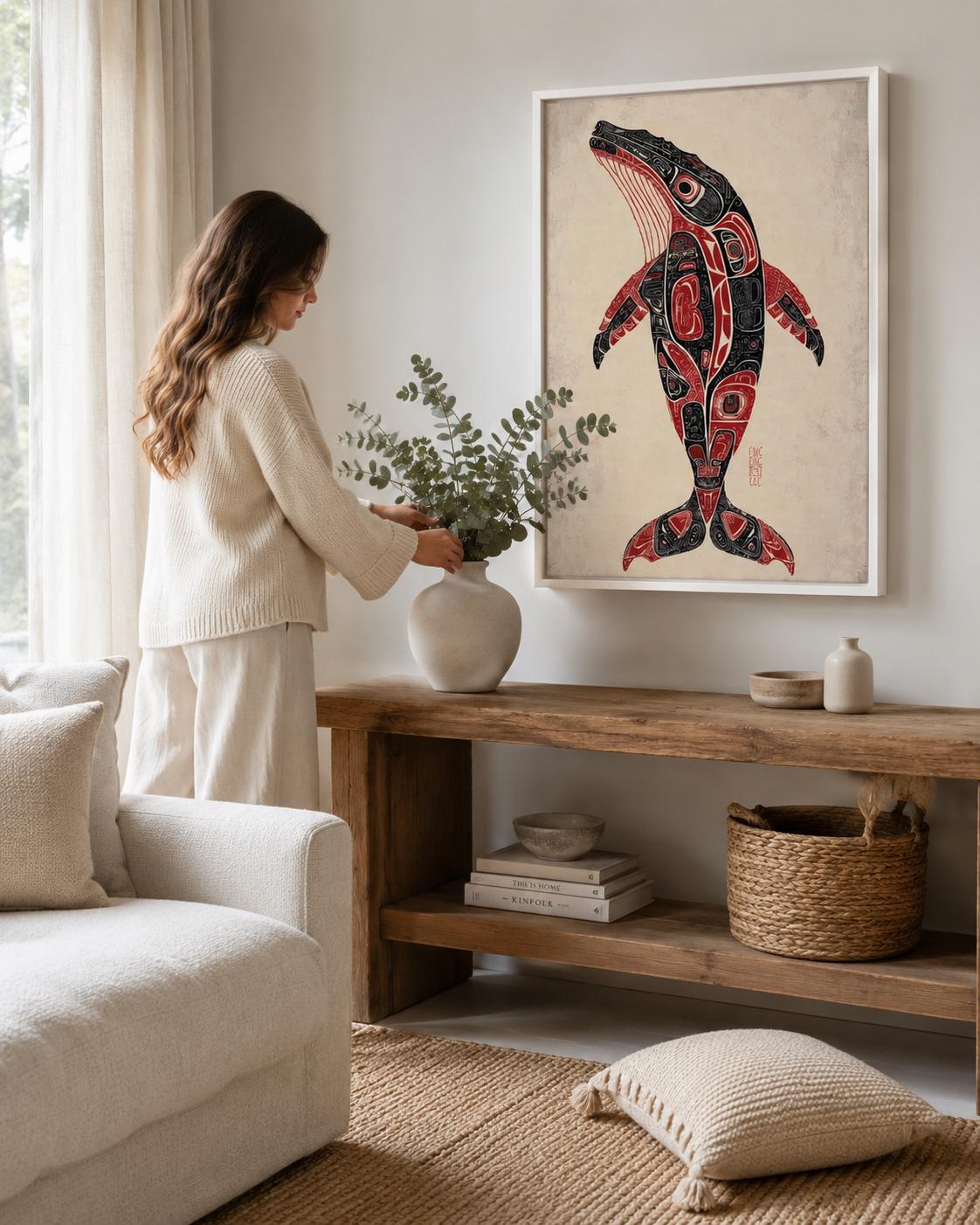Man holding a mug beside a framed whale artwork in a rustic cabin setting