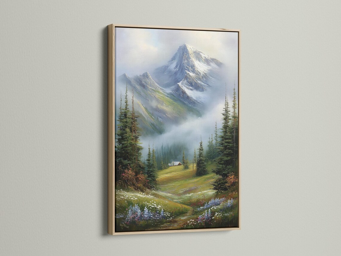 Room mockup showing a framed snowy mountain landscape painting with evergreen trees and a cabin