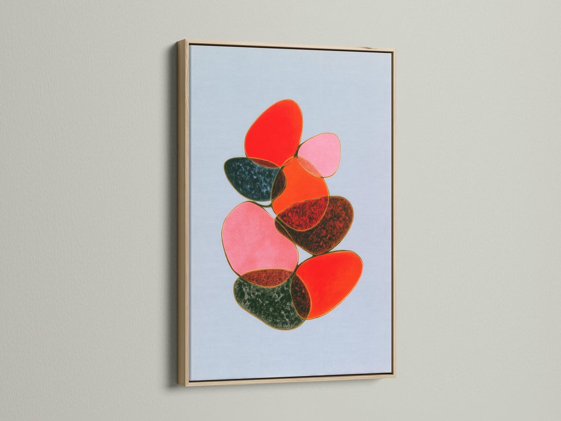 Room mockup showing a framed abstract artwork with overlapping red, pink and green shapes on a light blue background