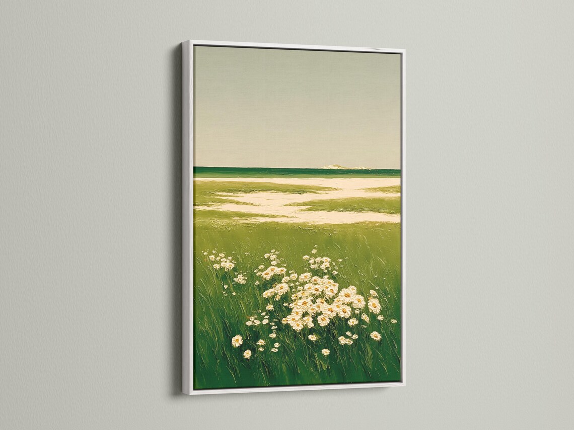 A framed landscape artwork on a light background wall showing green meadow grasses and cream flowers