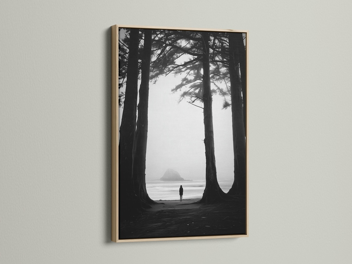 Monochrome seascape with dark tree trunks framing a foggy beach and a small lone figure detail view