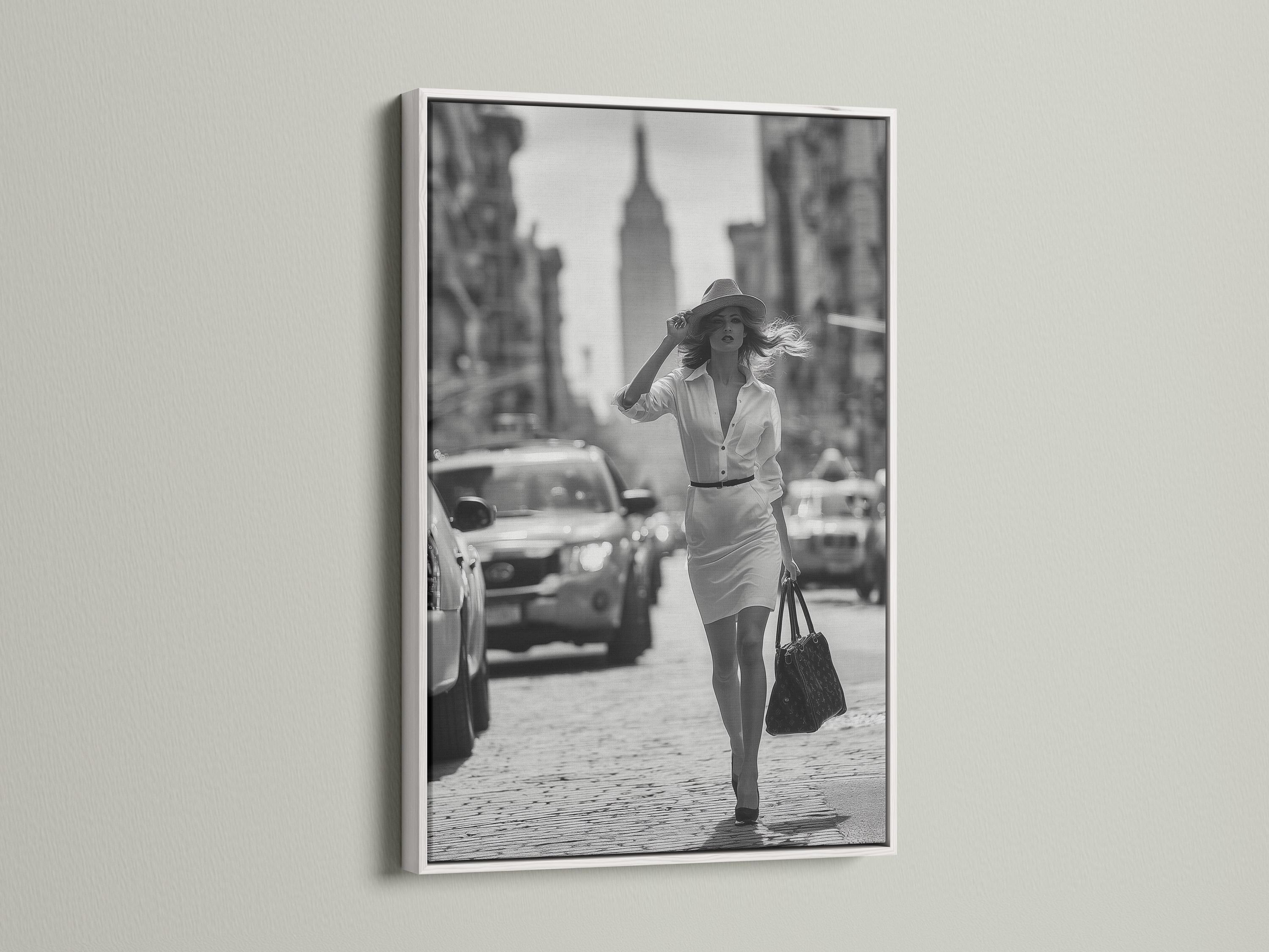 A black-and-white street photograph shows a stylish woman walking forward with a hat and handbag, with blurred city buildings and cars behind her