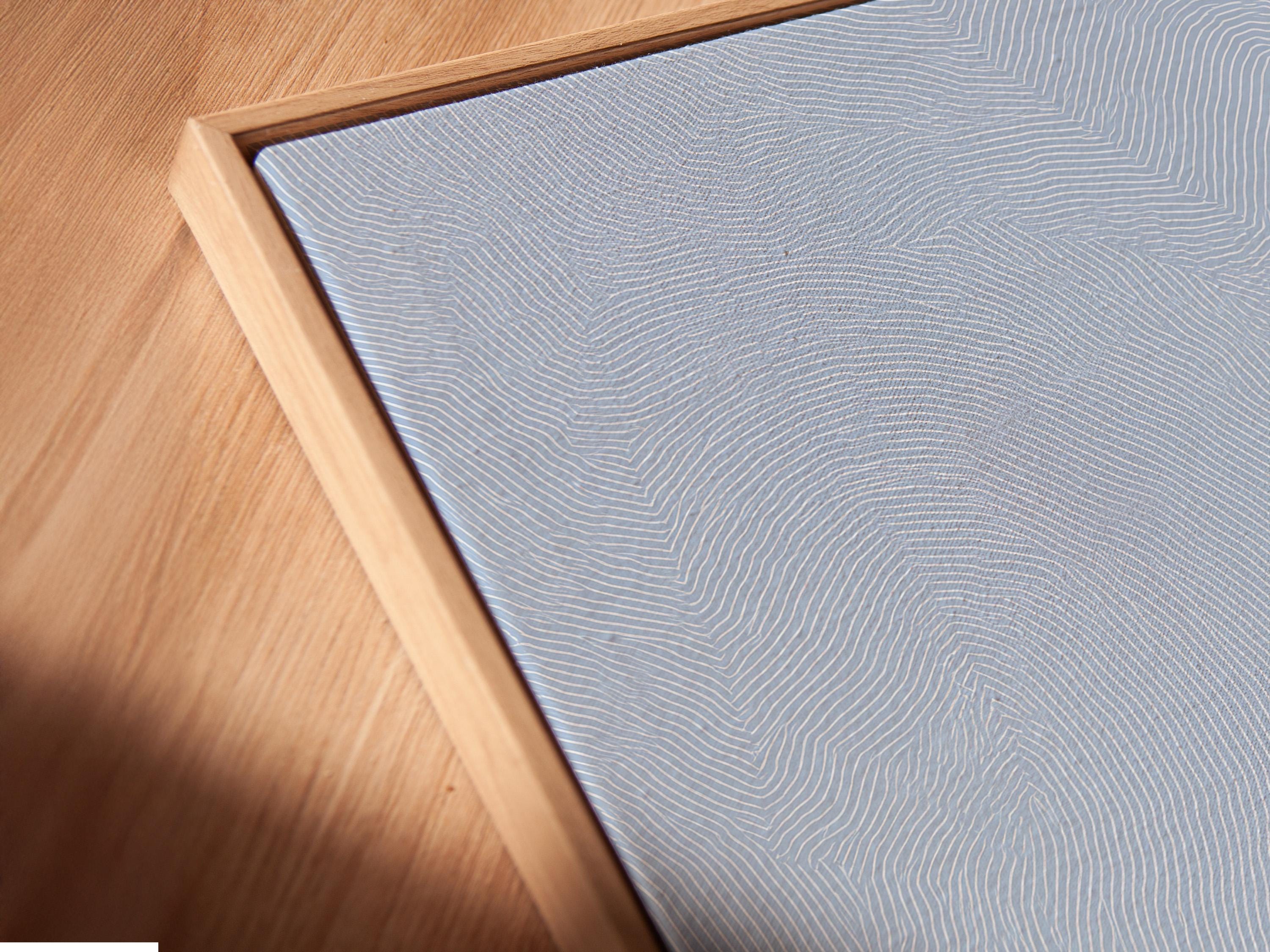 Room mockup showing a framed light blue minimalist seascape artwork with clouds and mountains