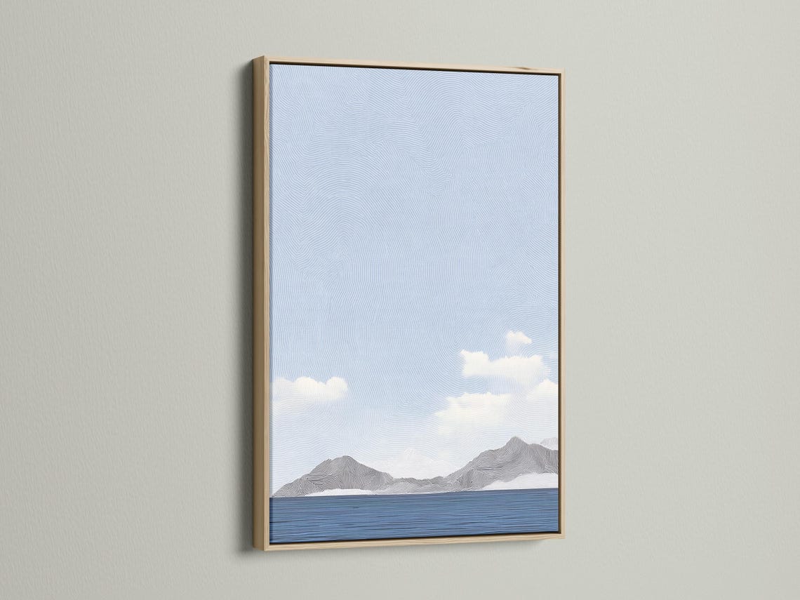 Room mockup showing a framed light blue minimalist seascape artwork with clouds and mountains