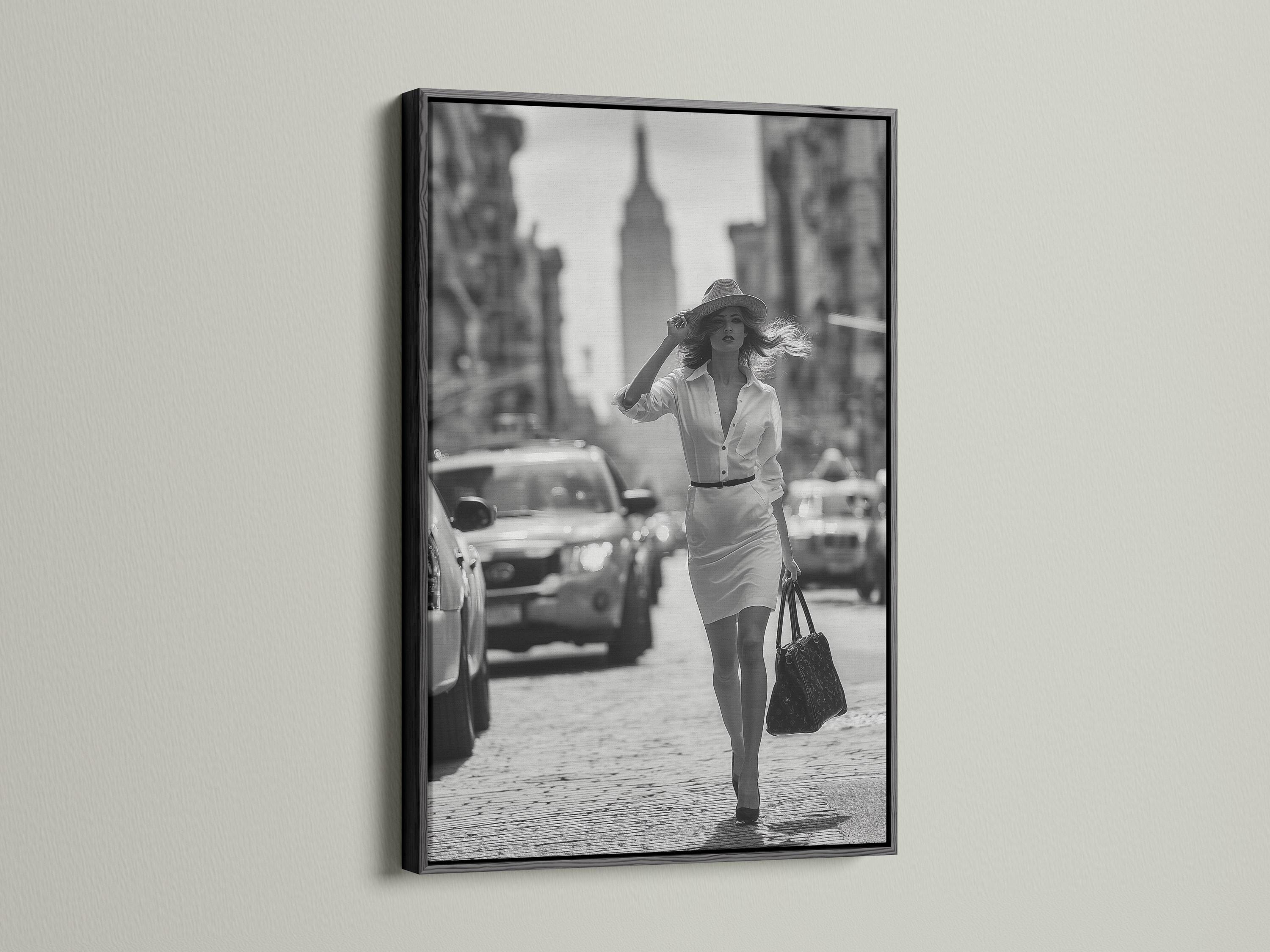 A black-and-white street photograph shows a stylish woman walking forward with a hat and handbag, with blurred city buildings and cars behind her