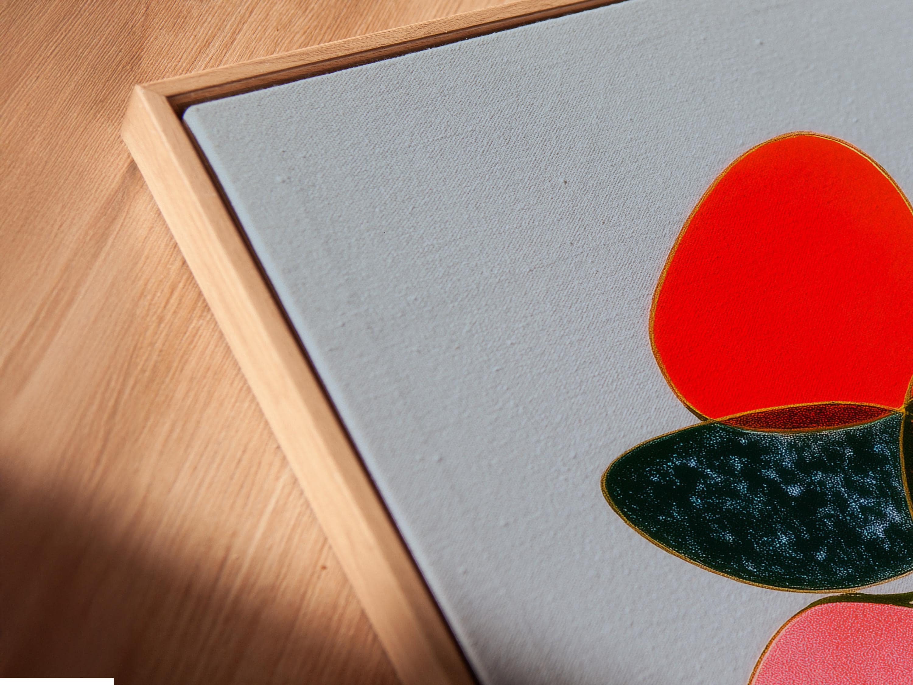 Room mockup showing a framed abstract artwork with overlapping red, pink and green shapes on a light blue background