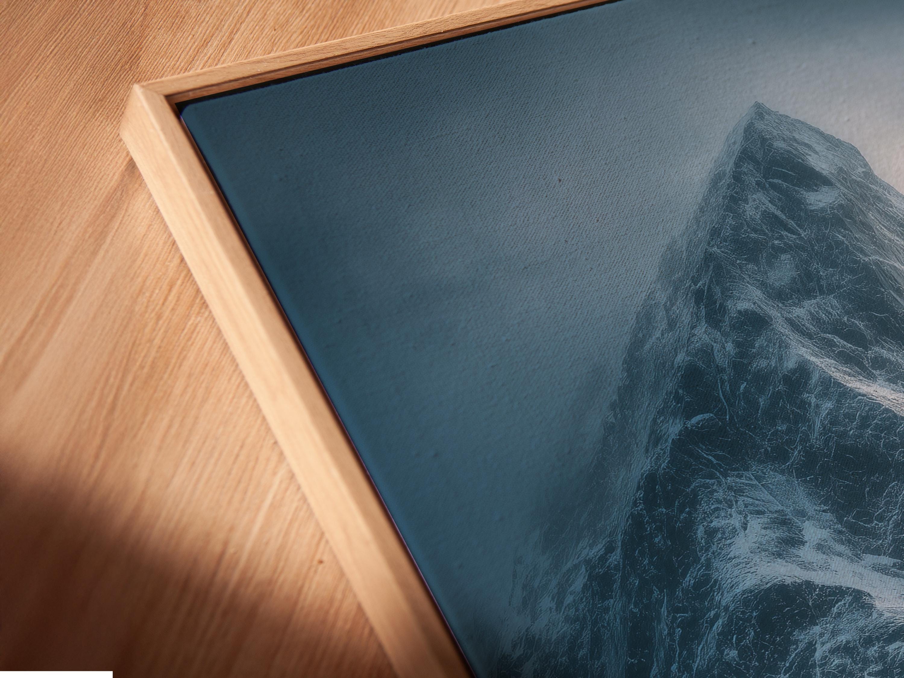 Blue misty mountain landscape with snow peaks, cloudy sky, and dark rocky shoreline detail view