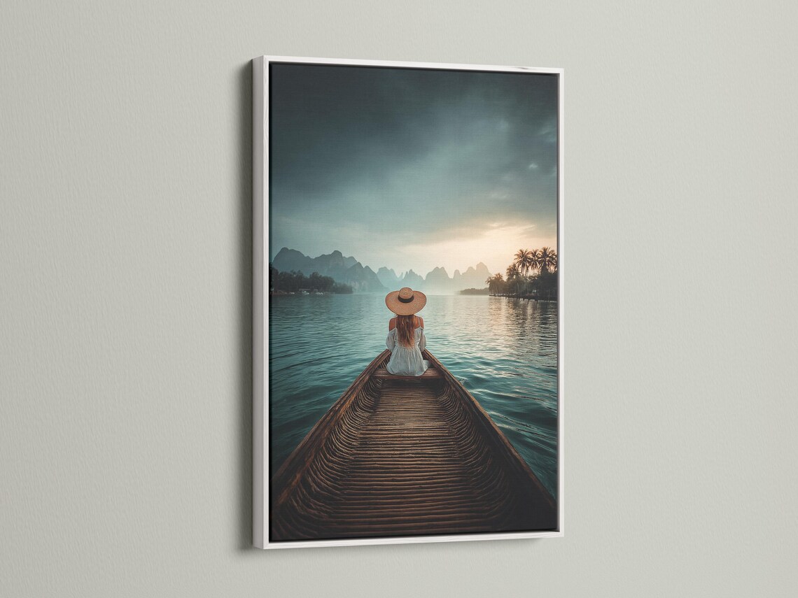 Woman in straw hat sits on a boat facing calm teal water, mountains and a warm sunrise sky detail view