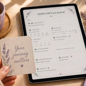 Peut inclure: Un journal de soins personnels pour le TDAH affiché sur une tablette, avec une carte indiquant "Your journey matters". Une tasse et un journal violets sont également visibles. Le journal est pour la réflexion quotidienne.