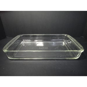 Könnte beinhalten: Eine rechteckige Backform aus klarem Glas mit integrierten Griffen an den kurzen Seiten. Der Boden der Form weist einen geprägten Text auf, der Pyrex, Made in USA und 232 lautet. Die Form hat glatte, abgerundete Kanten und eine transparente Oberfläche.