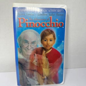 May include: A VHS tape for "The Adventures of Pinocchio" with Martin Landau and Jonathan Taylor Thomas. The cover features a blue background with the title in red and images of the characters. The tape is labeled "Limited Edition Magic Action Art."