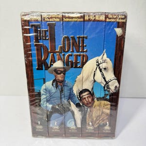 Può includere: Un cofanetto di cinque videocassette VHS di episodi di "The Lone Ranger". La scatola presenta immagini del Lone Ranger, un cavallo bianco e un altro uomo. I titoli degli episodi sono visibili nella parte superiore della scatola.