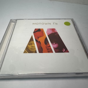 Puede incluir: Una caja de CD con el álbum "Motown 1's". La portada tiene un fondo blanco con el título en texto negro. La carátula del álbum incluye imágenes de músicos dentro de un logotipo "M" estilizado y colorido. Una pegatina verde está en la esquina superior derecha.