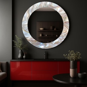 Puede incluir: Un espejo redondo con un marco decorativo nacarado cuelga sobre un mueble rojo. El marco del espejo presenta patrones arremolinados de blanco, dorado y colores iridiscentes. La habitación tiene paredes grises oscuras y una encimera negra.