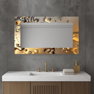 Può includere: Uno specchio rettangolare da bagno con un bordo dorato a forma di liquido. Lo specchio è montato sopra un piano di lavoro bianco con un lavandino integrato. Rubinetto e dispenser di sapone dorati sono anch'essi visibili.