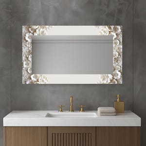 May include: A rectangular mirror with a white frame decorated with 3D floral details. The mirror is above a white countertop with a gold tap, soap dispenser, and folded towels. The wooden cabinet is below. The mirror is likely 100cm x 50cm.