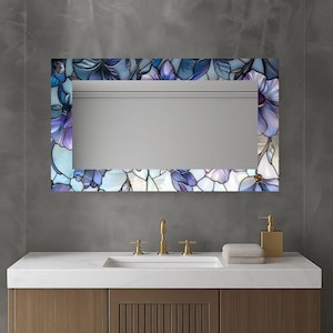 May include: Rectangular mirror with a floral stained glass border in shades of blue, purple, and white. The mirror is mounted above a white countertop with a gold faucet and soap dispenser.