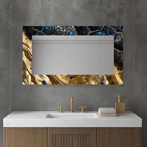 Puede incluir: Espejo rectangular de baño con marco decorativo. El marco presenta un patrón dorado similar a la veta de la madera en la parte inferior y los lados, que se transforma en un diseño veteado azul oscuro y dorado en la parte superior. El espejo está sobre una encimera blanca.