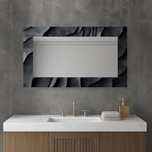 Può includere: Specchio rettangolare da bagno con cornice dal design grigio scuro a strati. Lo specchio è montato sopra un piano di lavoro bianco con un rubinetto e un dosatore di sapone dorati. Una pila di asciugamani piegati si trova a destra.