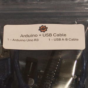 Peut inclure: Un sac en plastique transparent contenant un Arduino Uno R3 et un câble USB A-B. Une étiquette blanche sur le sac indique "Arduino + USB Cable" avec les composants listés. Ces composants sont pour des projets électroniques.
