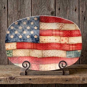 May include: Oval serving platter with a patriotic American flag design. The flag features a blue field with white stars and red and white stripes with a patchwork quilt aesthetic. The platter is displayed on a decorative metal stand.